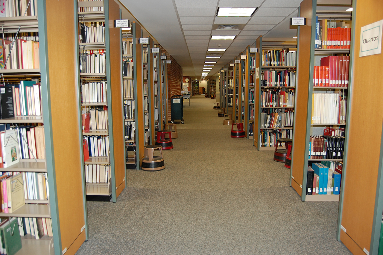Aisle between library shelves showing shelves going back in the distance