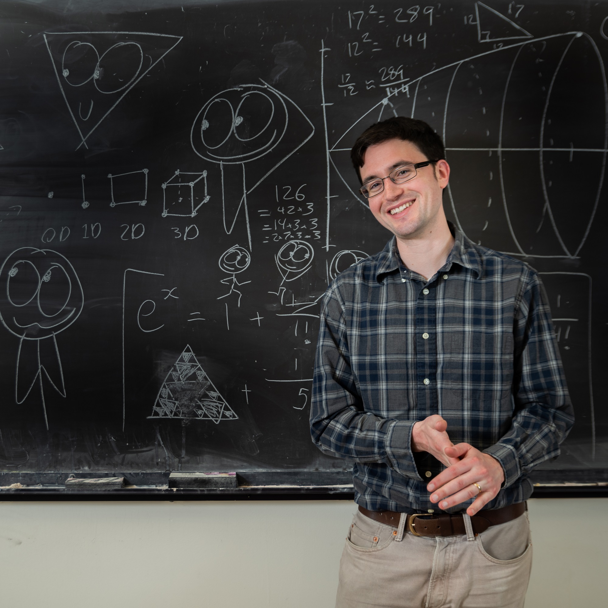 Ben Orlin smiling in front of a chalkboard with mathematics