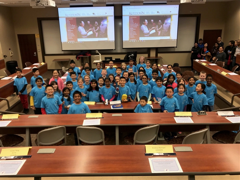 Math Kangaroo participants smiling in a group in the foreground with the event organizers in the back right