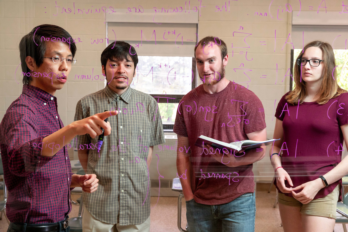 Professor explaining an equation written on a pane of glass to three students