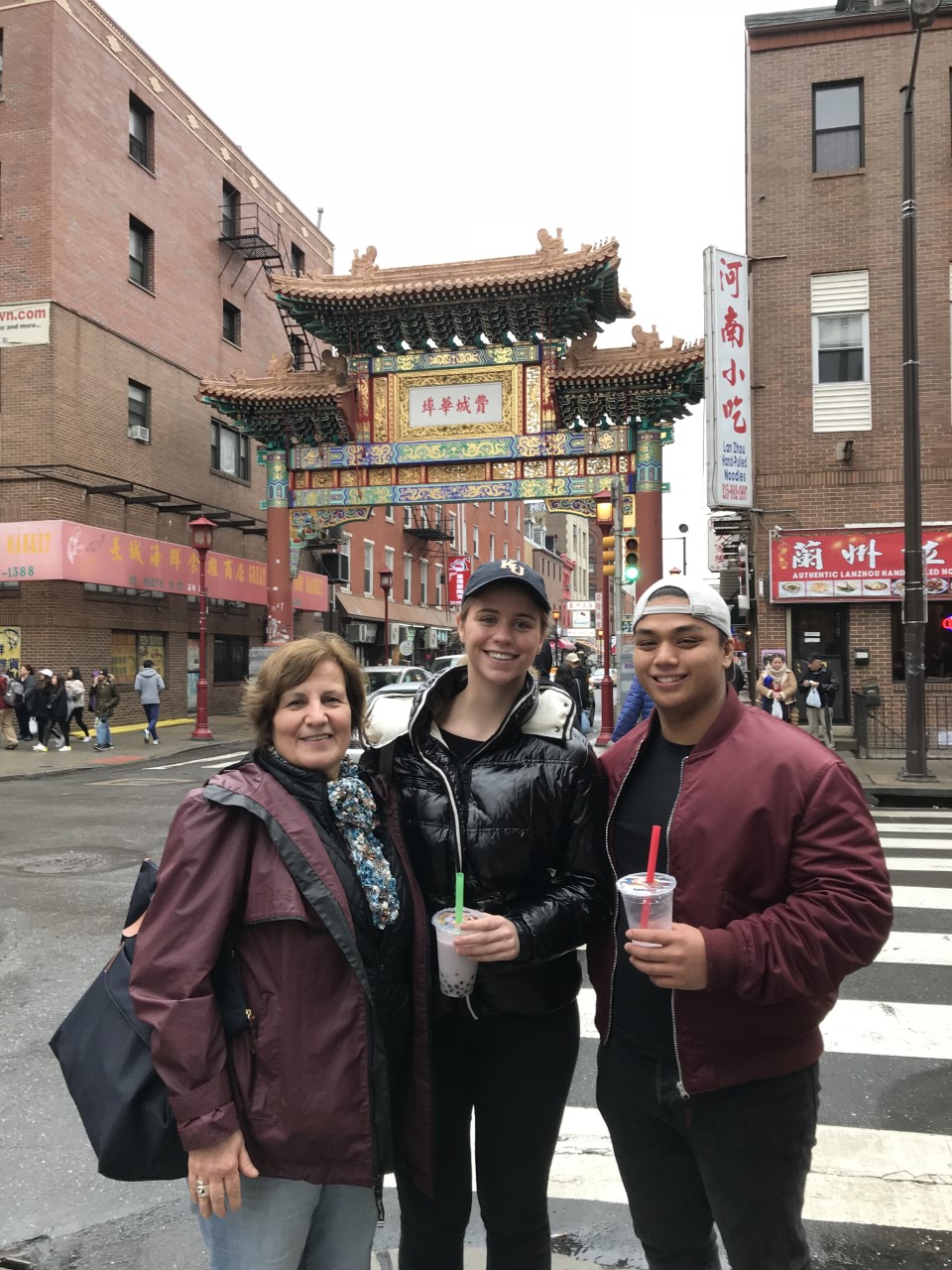 Two students and faculty advisor smiling and standing in front of a Philadelphia Chinatown street 
