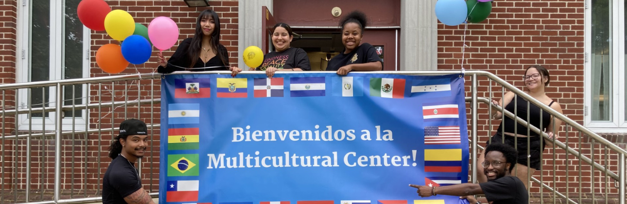 Six MCC students smile and point to MCC sign outdoors.