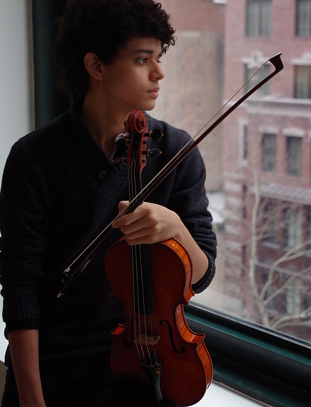 Alejándro Ortega holding the violin while looking out a window