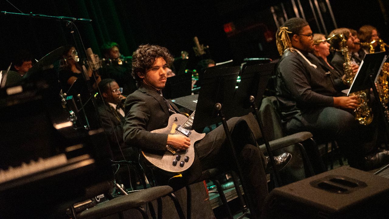 A side view of a large jazz ensemble with a seated guitar player in the foreground