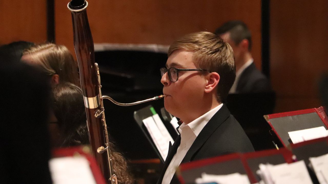 A bassoon player playing an orchestral concert surrounded by orchestral musicians and instruments on stage