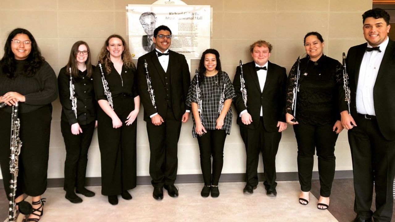 A group of clarinet students holding their instruments in front of a beige background