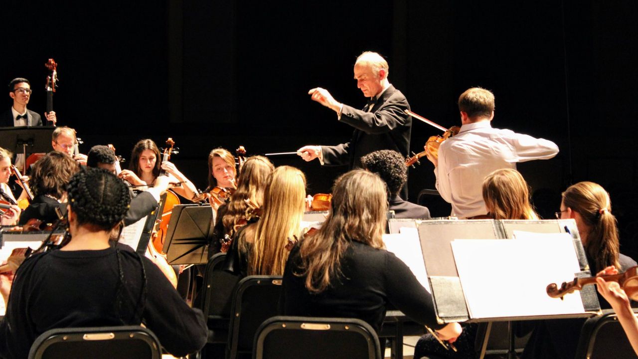 Orchestral musicians on stage performing with a conductor and soloist