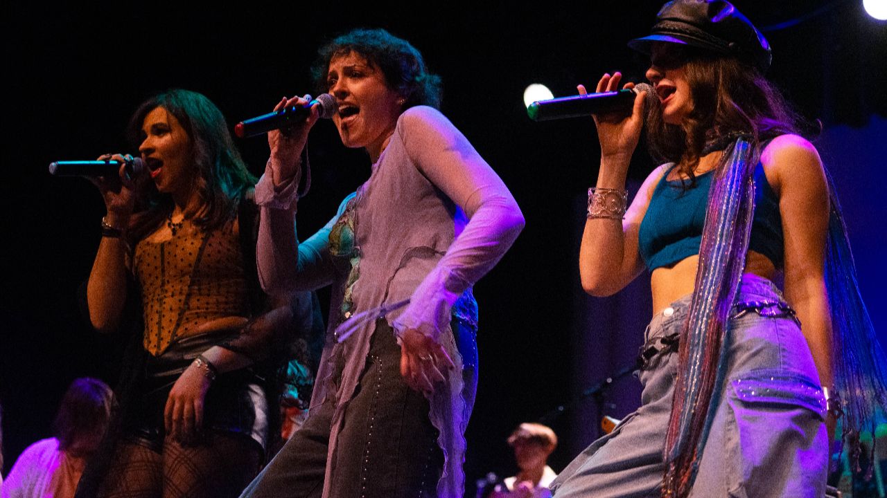 3 rock vocalists performing on stage with hands on microphones and hips