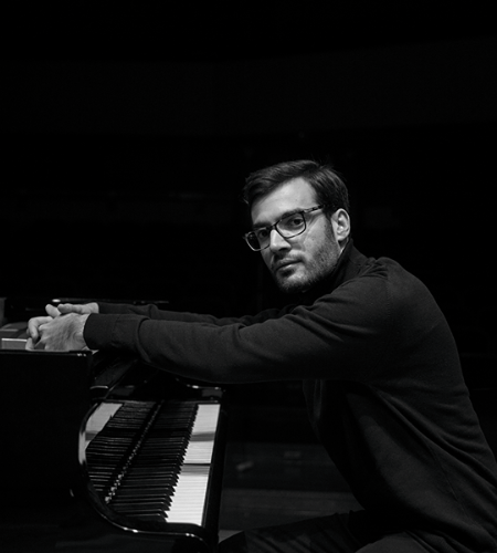 Professional photo of Dr. Athanasios Ramadanidis sitting at a piano against a black background