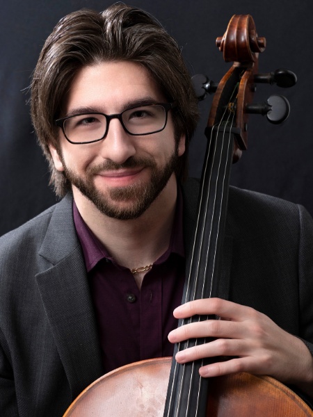 Dr. Julian Langford with glasses on, wearing a black suit with a maroon shirt and having cello in hand. 