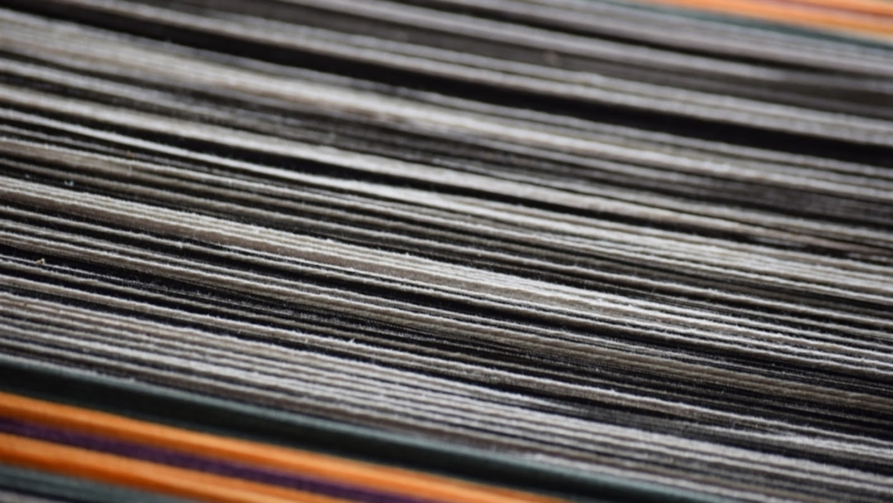 Black, white, yellow, green, and purple thread travel across the photo. These are the threads which make up the warp of a loom.