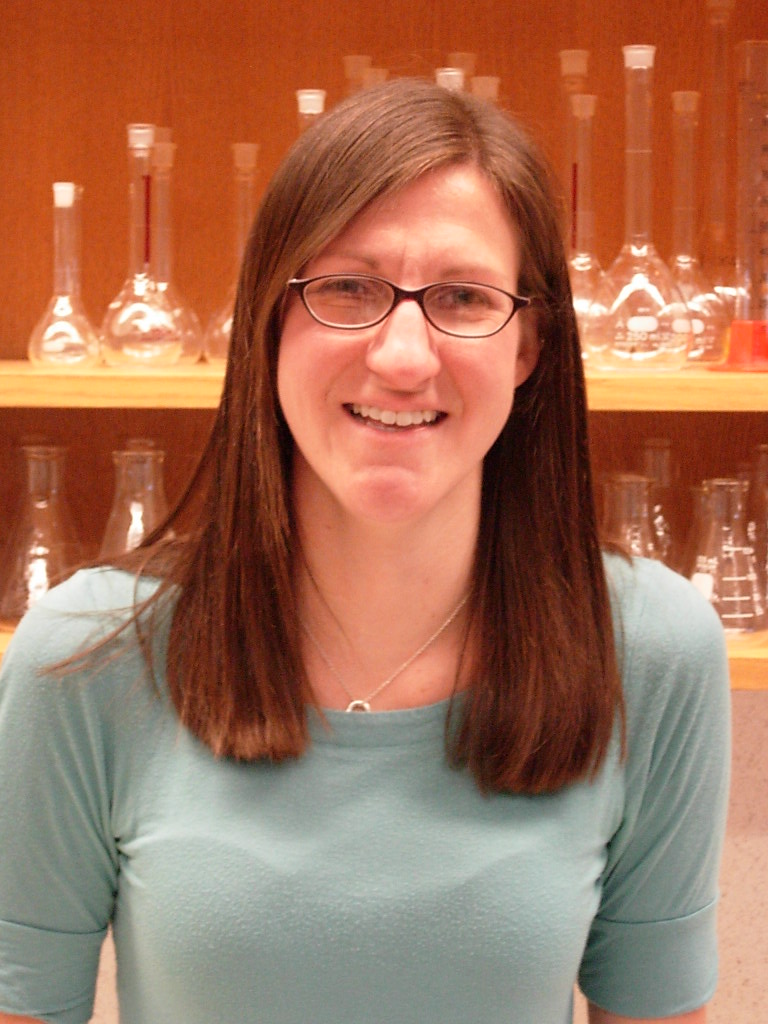 headshot of Dr. Palkendo with glasses in front of chemistry glassware on shelves
