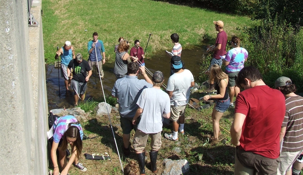 Geology class wading in a small, overflowing creek and using flood assessment equipment