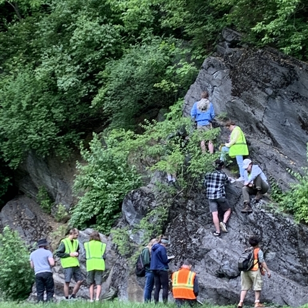 Students wearing neon vests climbing up the side of a cliff 