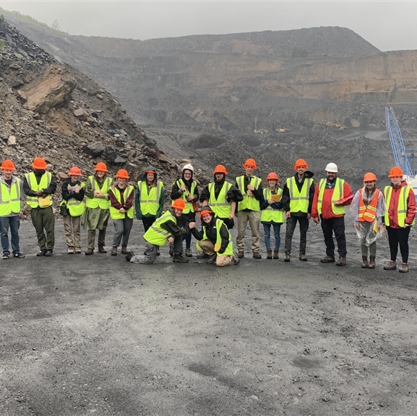 Class of students standing in front of a mountain, wearing neon hard hats and vests 