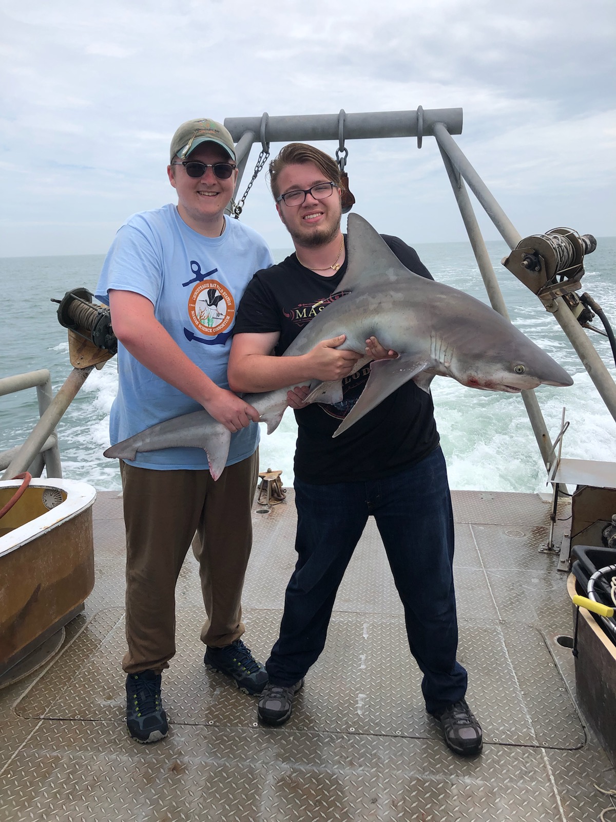 Two KU Students holding a shark on the deck of a boat