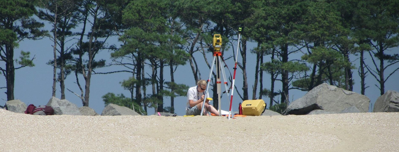 Student sitting on the beach behind profiting gear, analyzing the area.