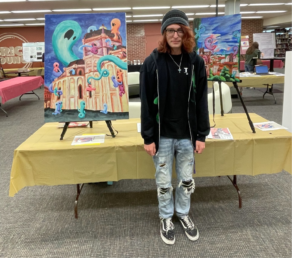 student standing in front of two works of art presenting at KU Inspires event