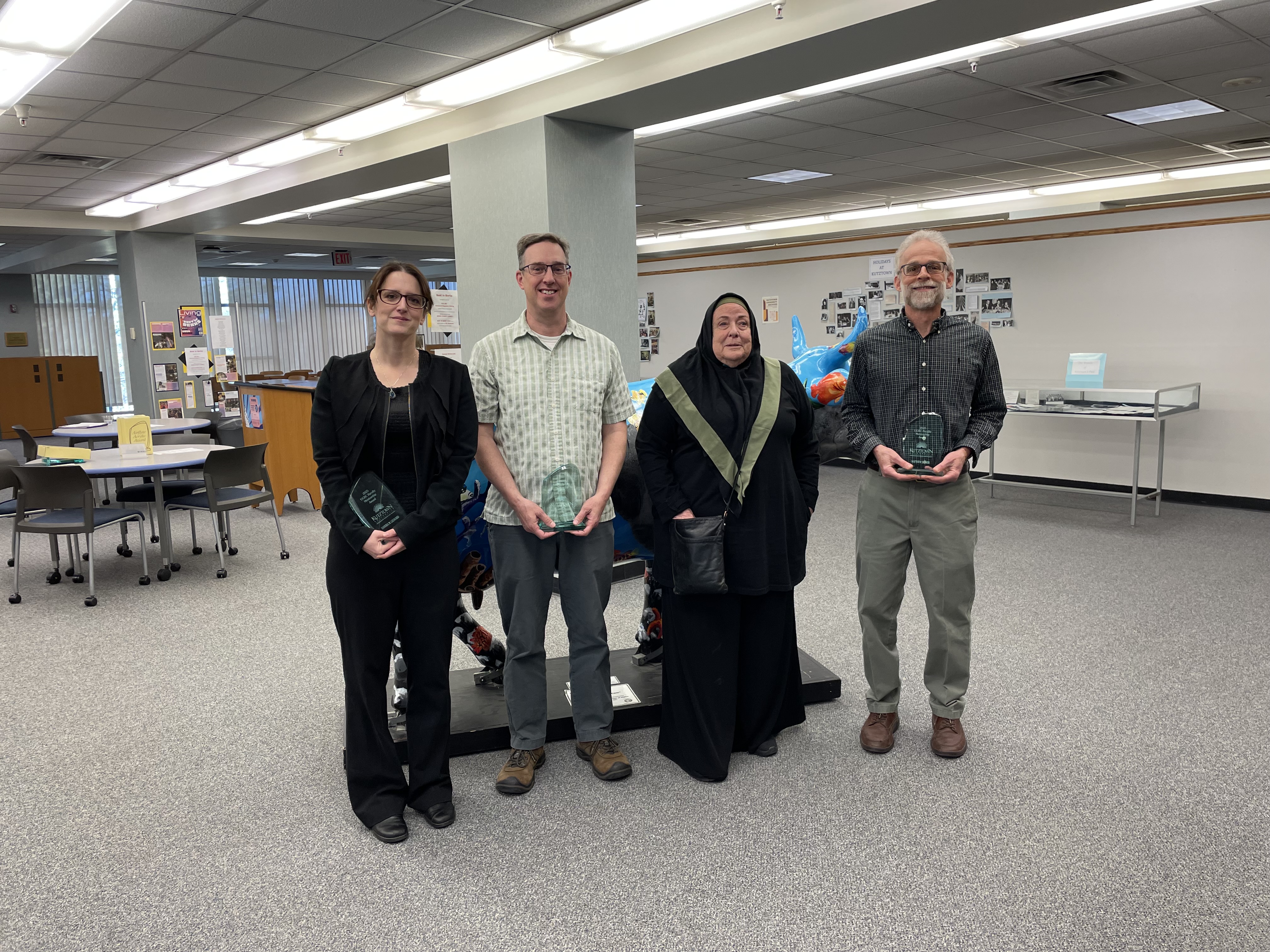 Four people posing for group photo, gray floor and background