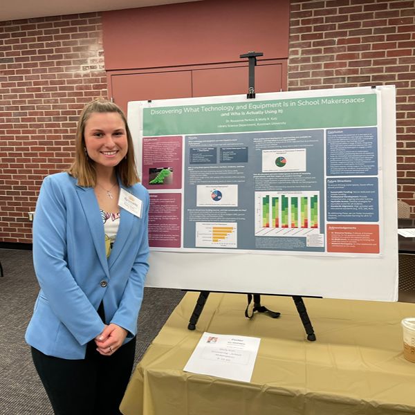Student in blue blazer smiles in front of their poster