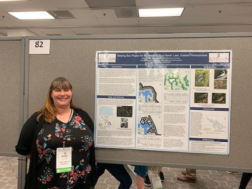 Maria Smoyer presents at 2019 meeting, smiling next to her presentation poster