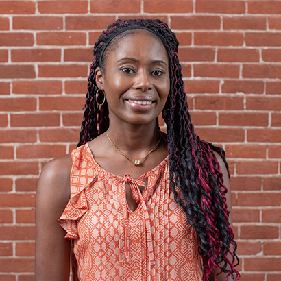 Image of Veronne Demesyeux in orange blouse in front of brick background