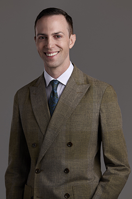 Image of Zachary Adams in brown/grey jacket in front of grey background