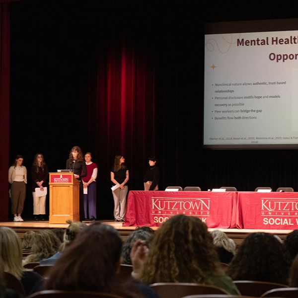 K.U. Students presenting on stage in Schaeffer Auditorium in front of projecting screen