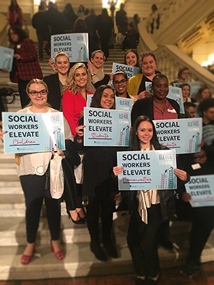 Students standing on a staircase holding signs that say "social workers elevate" at Lead Day 2019