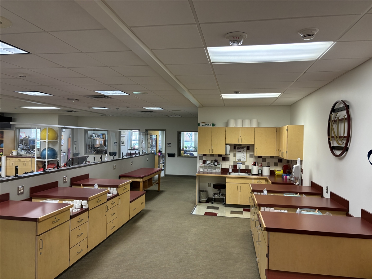 Medical tablesand stacks of medical tape in the foreground, with a handwashing station and medicine cabinets in the background