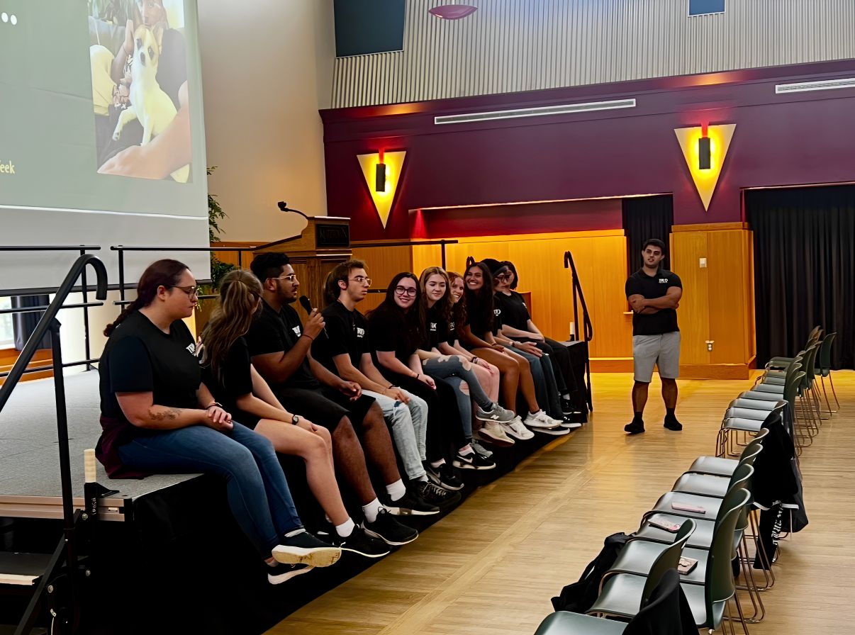 TRIO Mentors sitting on a stage with the TRIO Graduate assistant standing to the side.