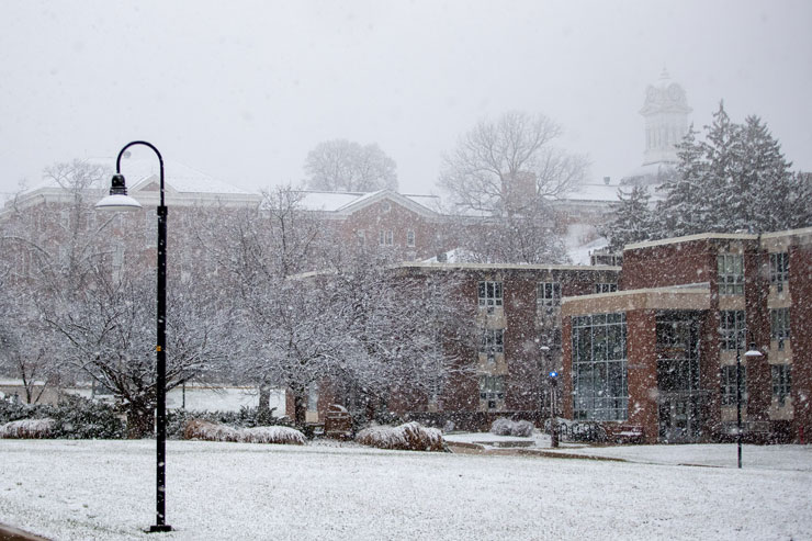 Snowy scene with Beck Hall in the forefront and the clock tower, barely visible through the snow, in the background. 
