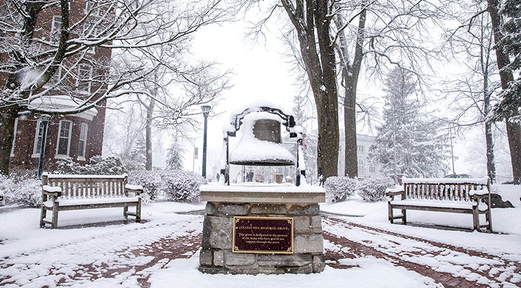 College Hill Memorial Plaza with Schaeffer Auditorium barely visible in the background through the falling snow. Patches of red brick can be seen where snow is yet to stick. 