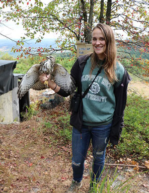 Image of Chelsea Johnson in wooded area holding broad-tailed hawk.
