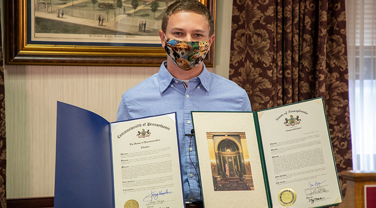 Male student Daniel Johns wearing a mask and holding his awards