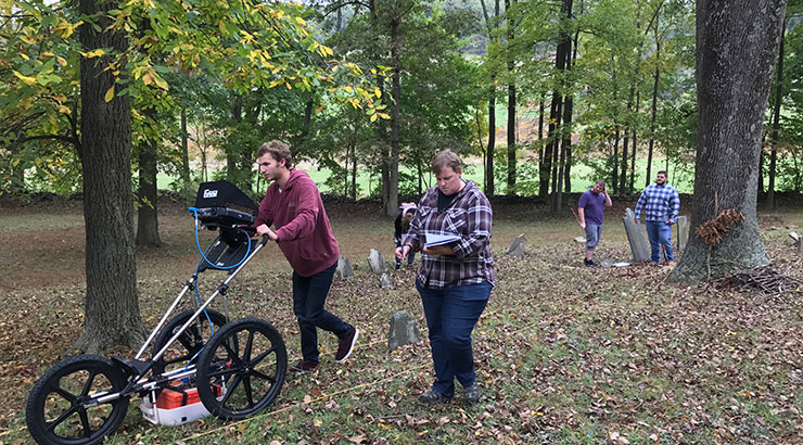 Undated image of four geology students conducting field research in a wooded area in early fall. 