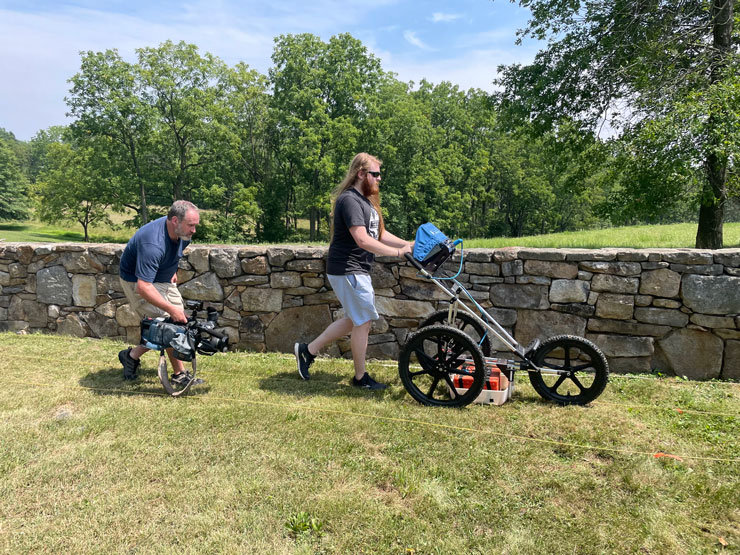 Photo of two members of the Geophysics Society pushing equipment across the grass.