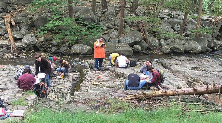 In an undated photo, geology students conduct field studies along a boulder and rock creek bed in the woods. 