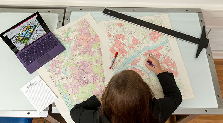 Overhead shot of a student tracing bylines on several large regional maps 