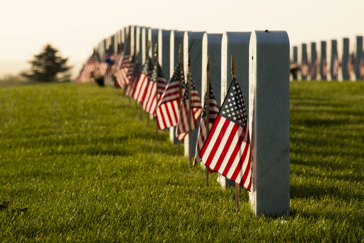 Row of tombstones in national cemetery adorned with United States of America flags. 
