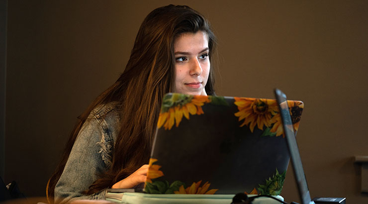 Female student sitting at a laptop printed with sunflowers, taking an online class