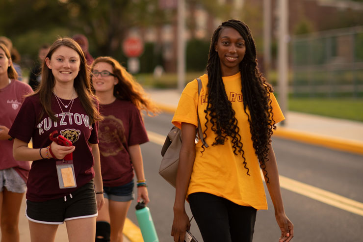Students walk along Main Street during a campus tour. Two students in front of group, look towards the camera with smiles. 