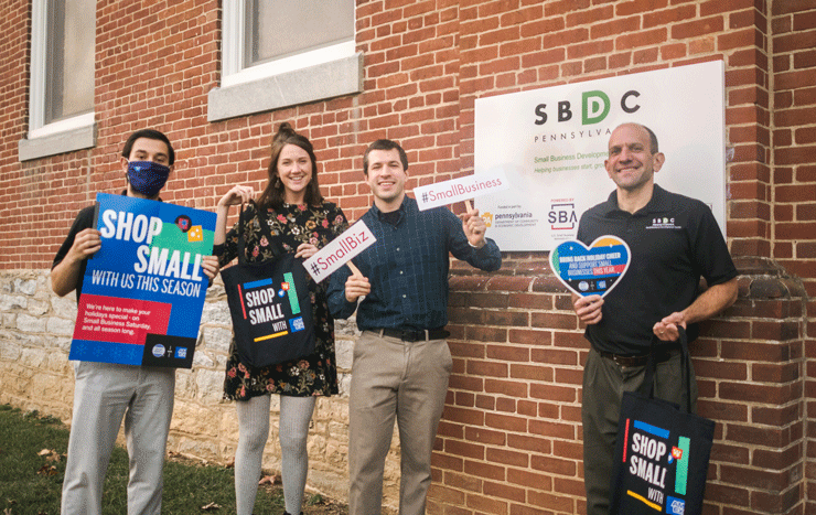 A group of four people holding Shop Small Business Saturday, SBDC and #ShopSmallPA signs.