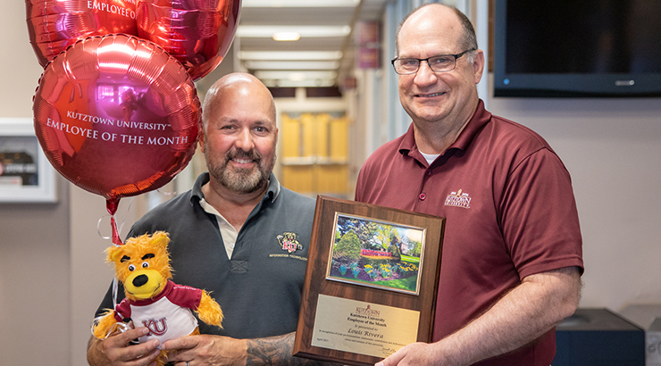 Photo of Louis Rivera (left) standing with President Hawkinson (right). Lou is holding balloons, stuffed Avalanche. Dr. Hawkinson holds the award plaque.
