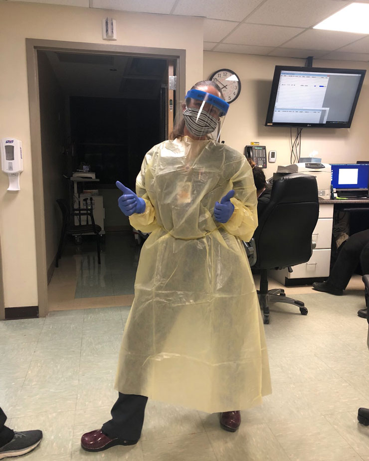 Shannah Steel dressed in personal protective equipment in a hospital emergency room giving two thumbs up.