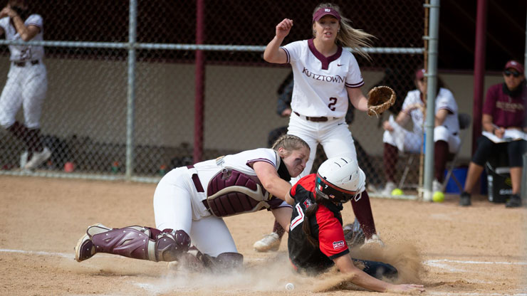 Kutztown University's softball catcher makes play at home plate against ESU. KU player wearing #2 stands behind ready to back up play. 