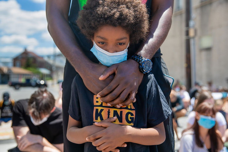 Image of a person with their arms around an African American child standing at a Black Lives Matter march in Kutztown, Pennsylvania. The child's face showing thoughtful and sad emotion.