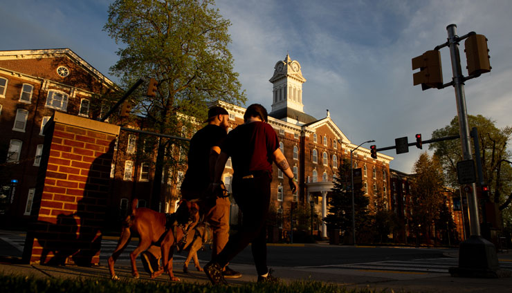 Photo of two individuals walking with two dogs in front of Old Main
