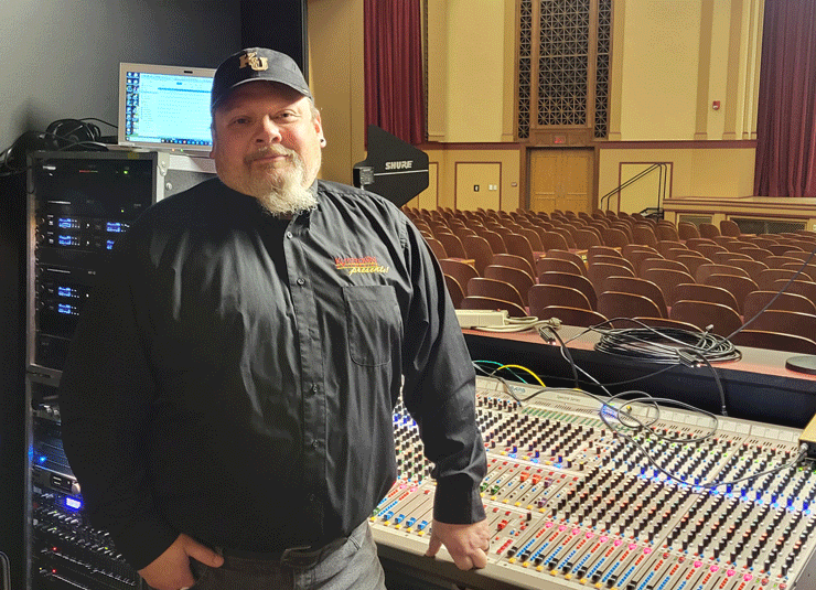 A photo of KU's new production coordinator, Tim Shapiro, standing at the sound board in Schaeffer Auditorium.