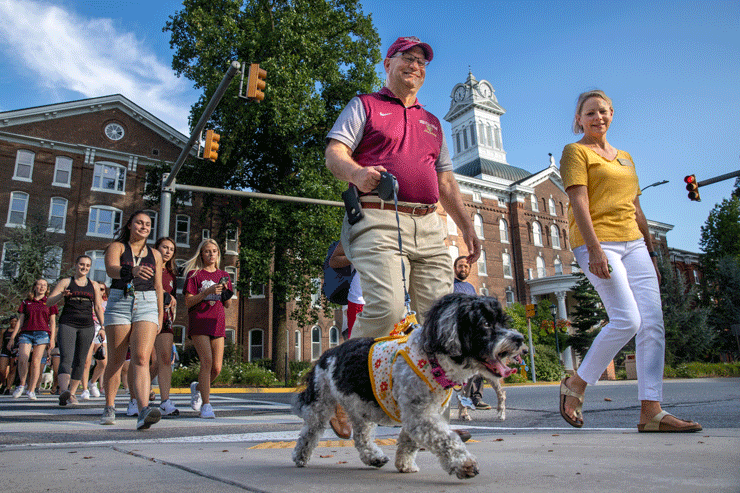 President Kenneth Hawkinson, Mrs. Hayes-Hawkinson, and their dog, Wynnie walk with a group of students. 